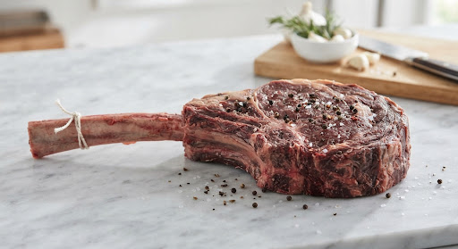 Massive French-trimmed dry aged Halal tomahawk rib steak with long exposed rib bone on marble counter